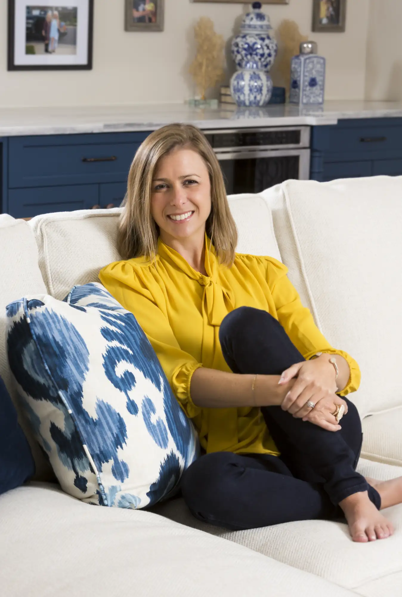 Interior Designer Lauren Nicole Clement smiles while sitting comfortably on a white sofa against a background of custom blue cabinetry and white porcelain decor.