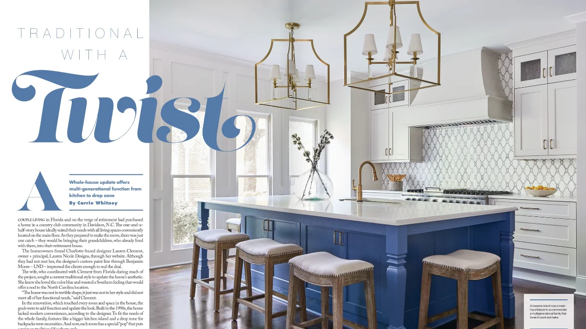 A two-page magazine spread showing a bright kitchen features a large royal blue island with a white marble top and four wooden stools. Brass fixtures and two geometric pendant lights hang over the workspace.