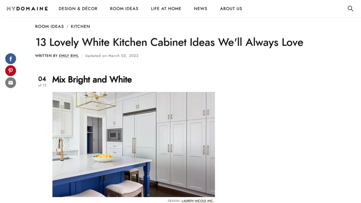 A screenshot of the MYDOMAINE article featuring a white kitchen featuring tall paneled cabinets and a large island painted in bright cobalt blue, topped with white stone.