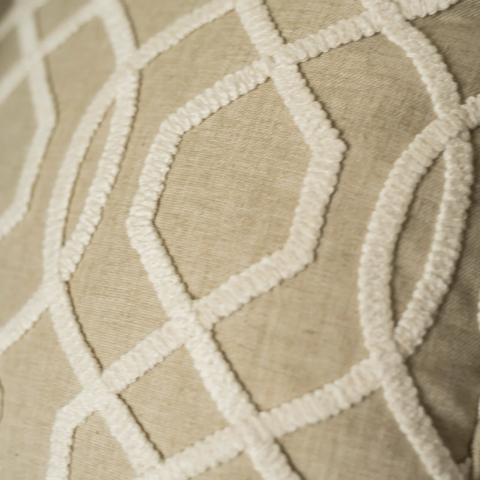A close-up view of a beige linen-look fabric embroidered with a thick, raised white geometric trellis pattern.