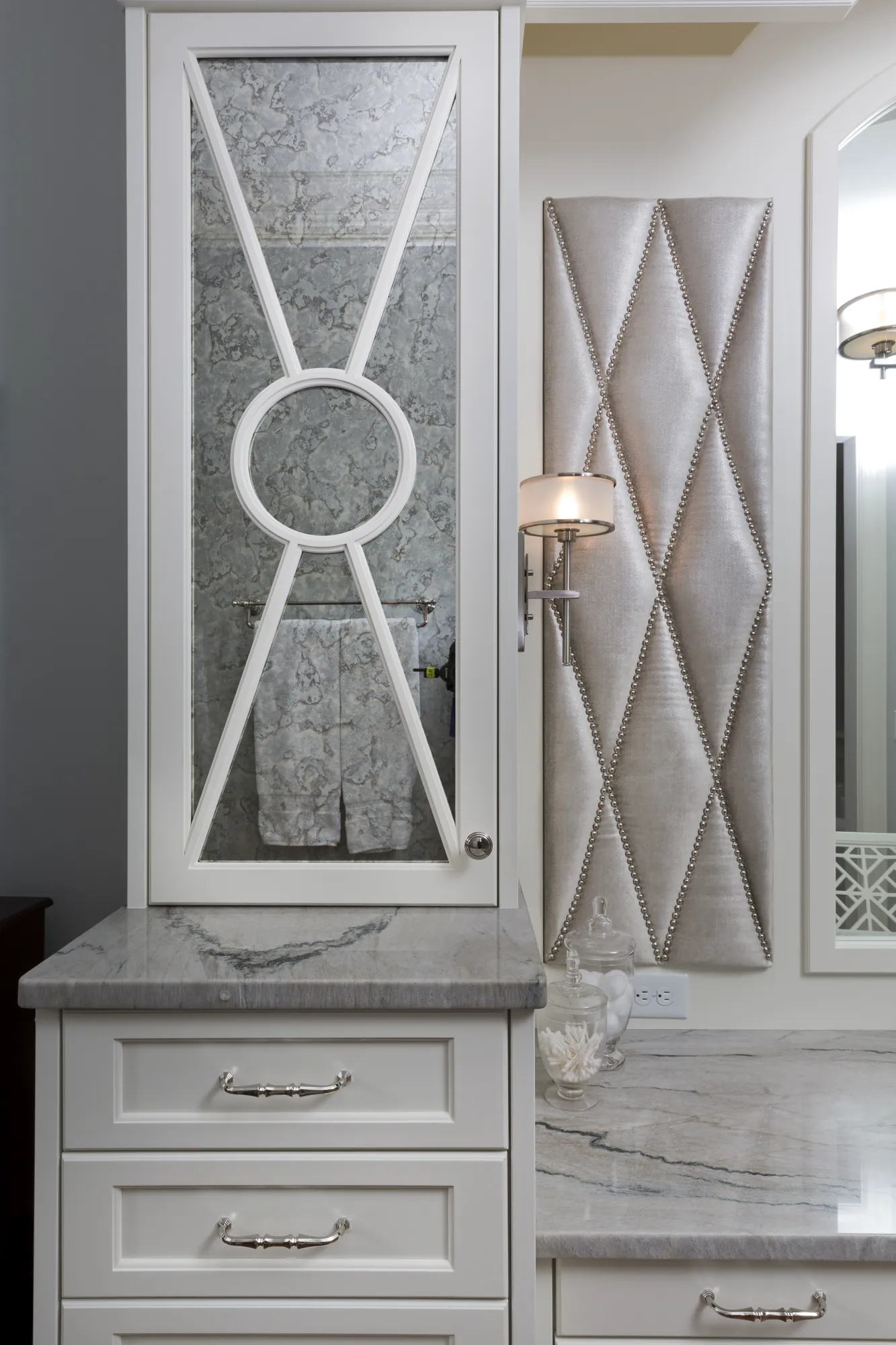 Elegant bathroom featuring white custom cabinetry, a marble counter, and a tufted silver wall panel framed by cabinet structures.
