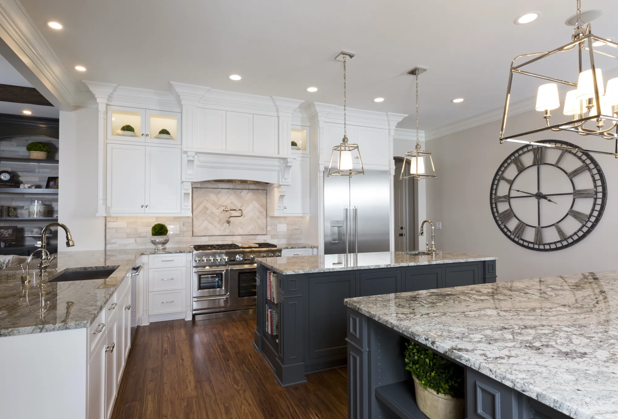 A bright, modern kitchen with white cabinets, stainless appliances, and dark gray islands. Light granite countertops, wood floors, and decorative lighting create a refined space.