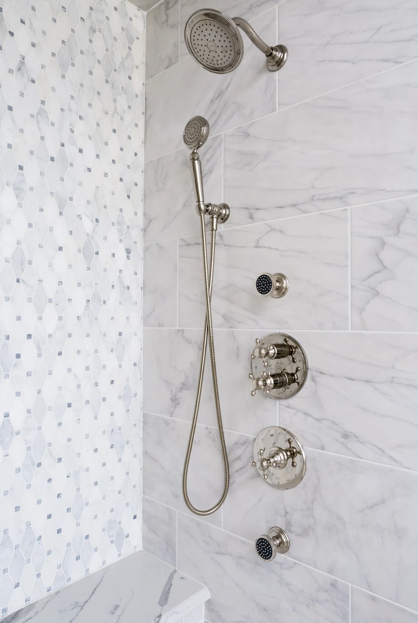 A luxurious shower detailed with large white marble tiles and a patterned mosaic accent wall. The polished nickel fixtures include an overhead shower and body sprays.