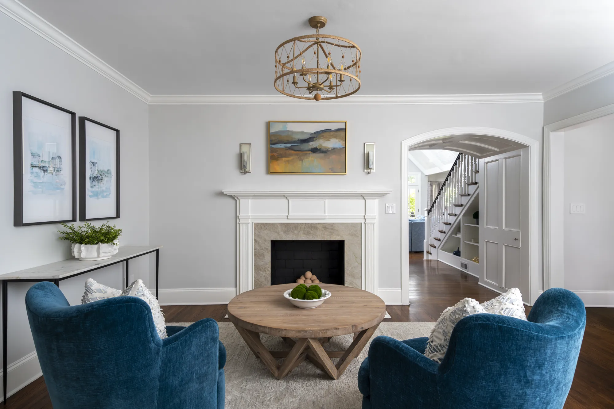 Two deep blue velvet armchairs frame a round natural wood coffee table and a decorative white fireplace mantel in a stylish, symmetrical sitting room.