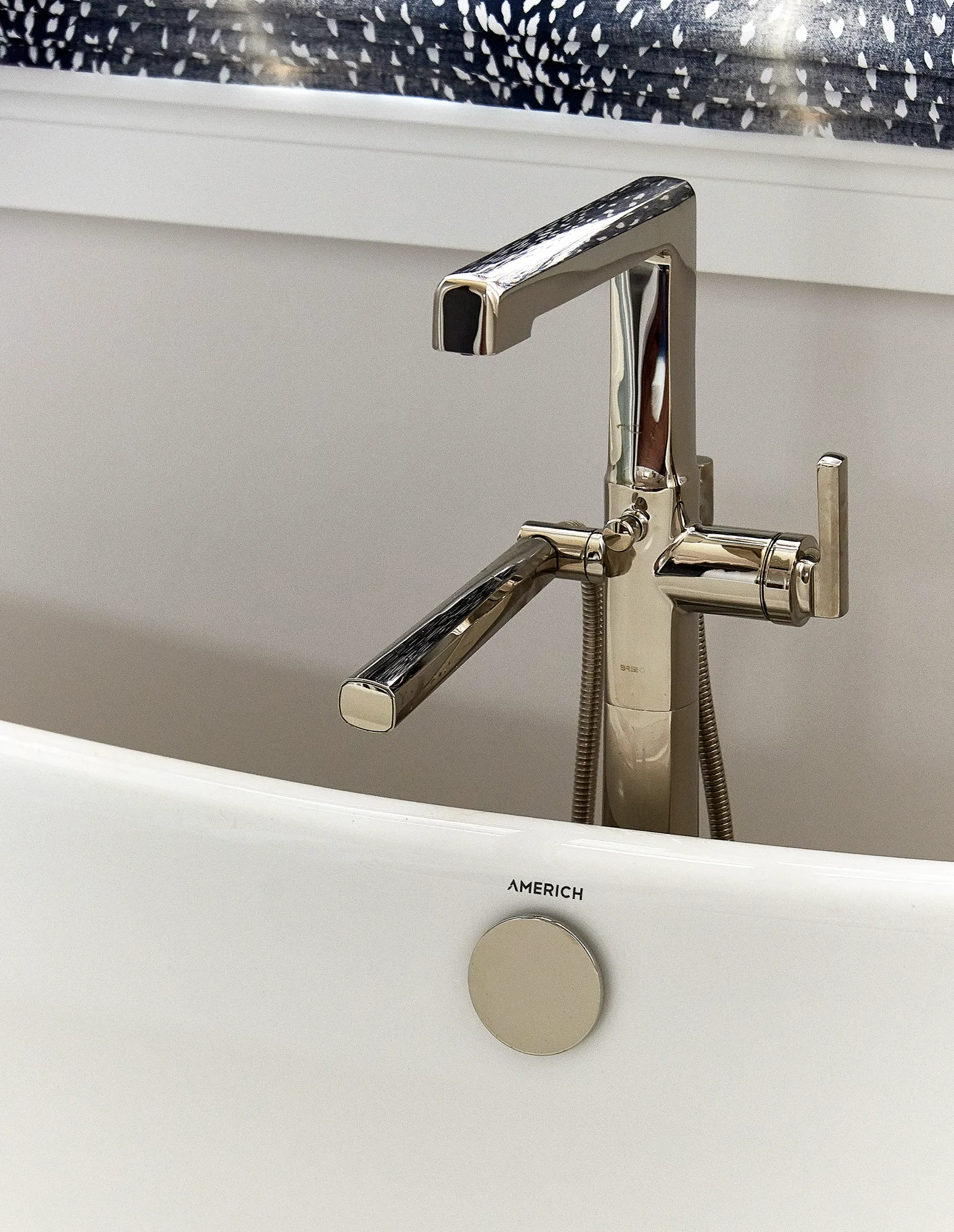 A contemporary polished nickel tub filler faucet installed on a white freestanding bathtub.
