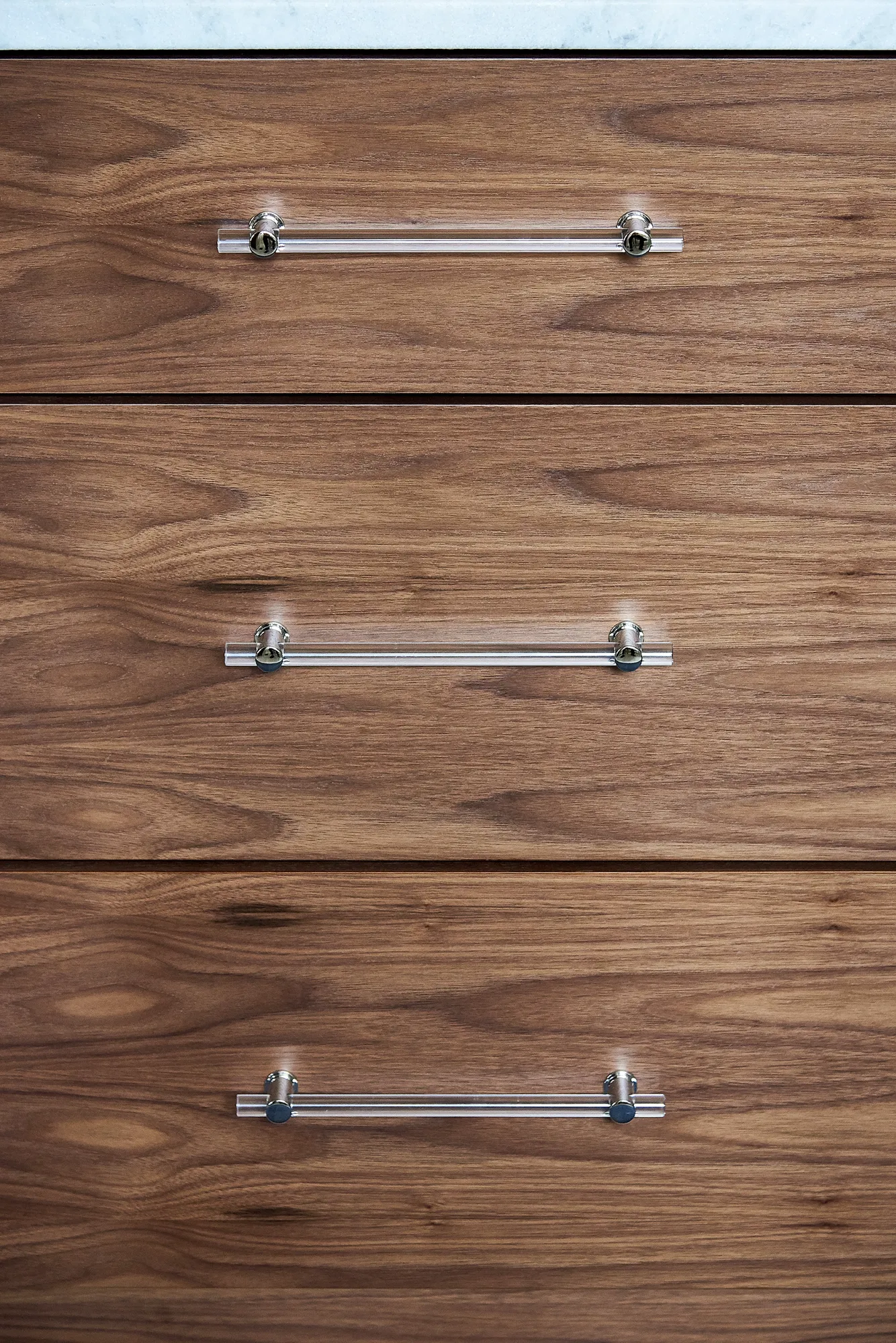 A vertical close-up of three dark wood drawers with clear cylindrical acrylic handles and polished chrome mounts.