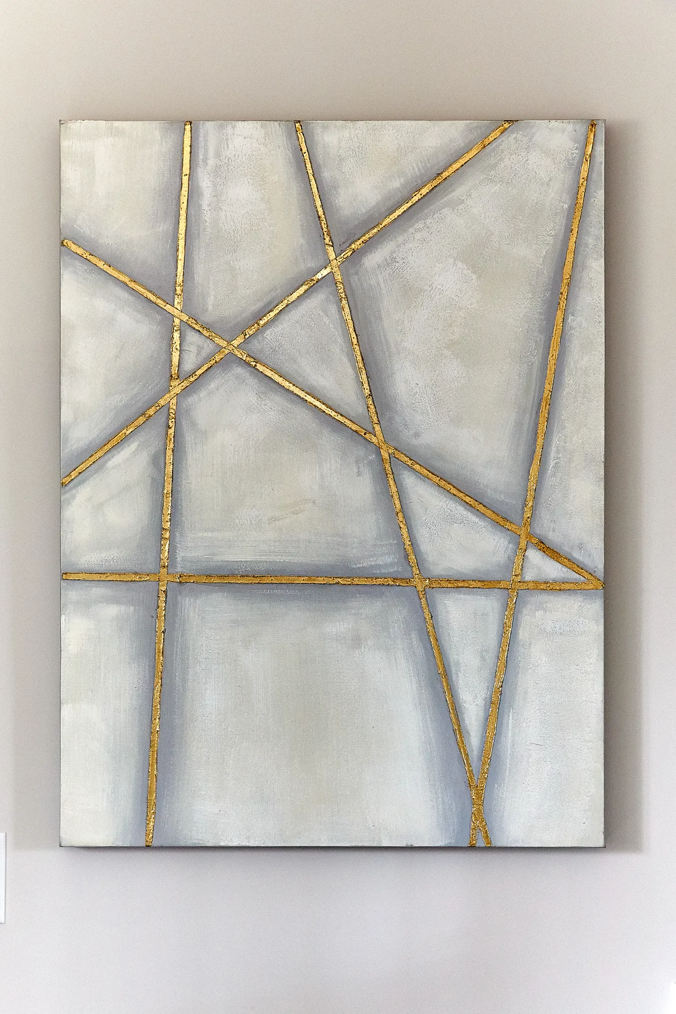 An abstract artwork with geometric gold lines intersecting across a lightly textured canvas painted in subtle shades of gray and white.