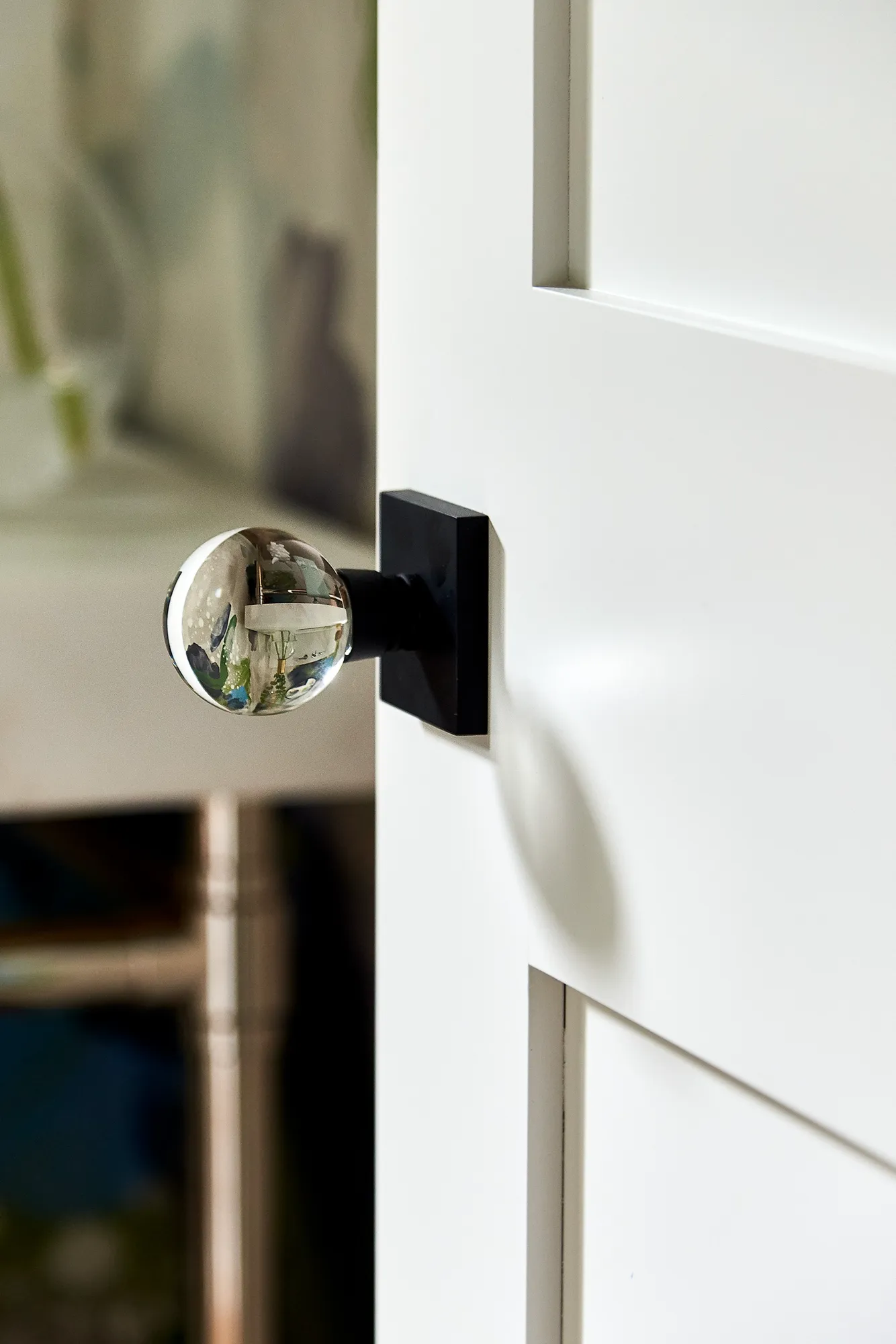 A modern, clear crystal globe door knob on a matte black plate, set into a white paneled interior door.