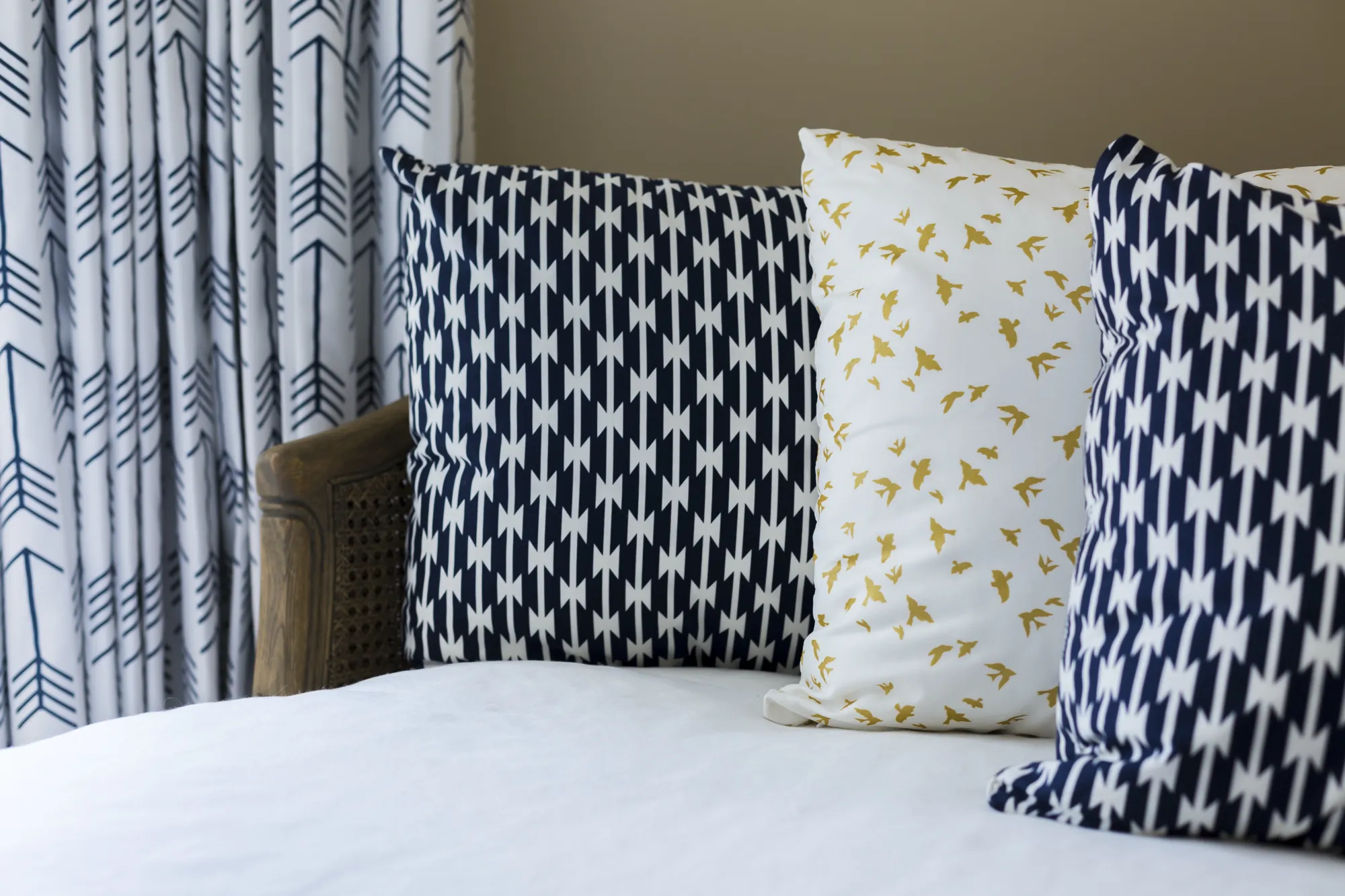 A pair of navy and white patterned pillows, one white gold-bird pillow, and coordinated arrow curtains create a stylish look on a daybed.