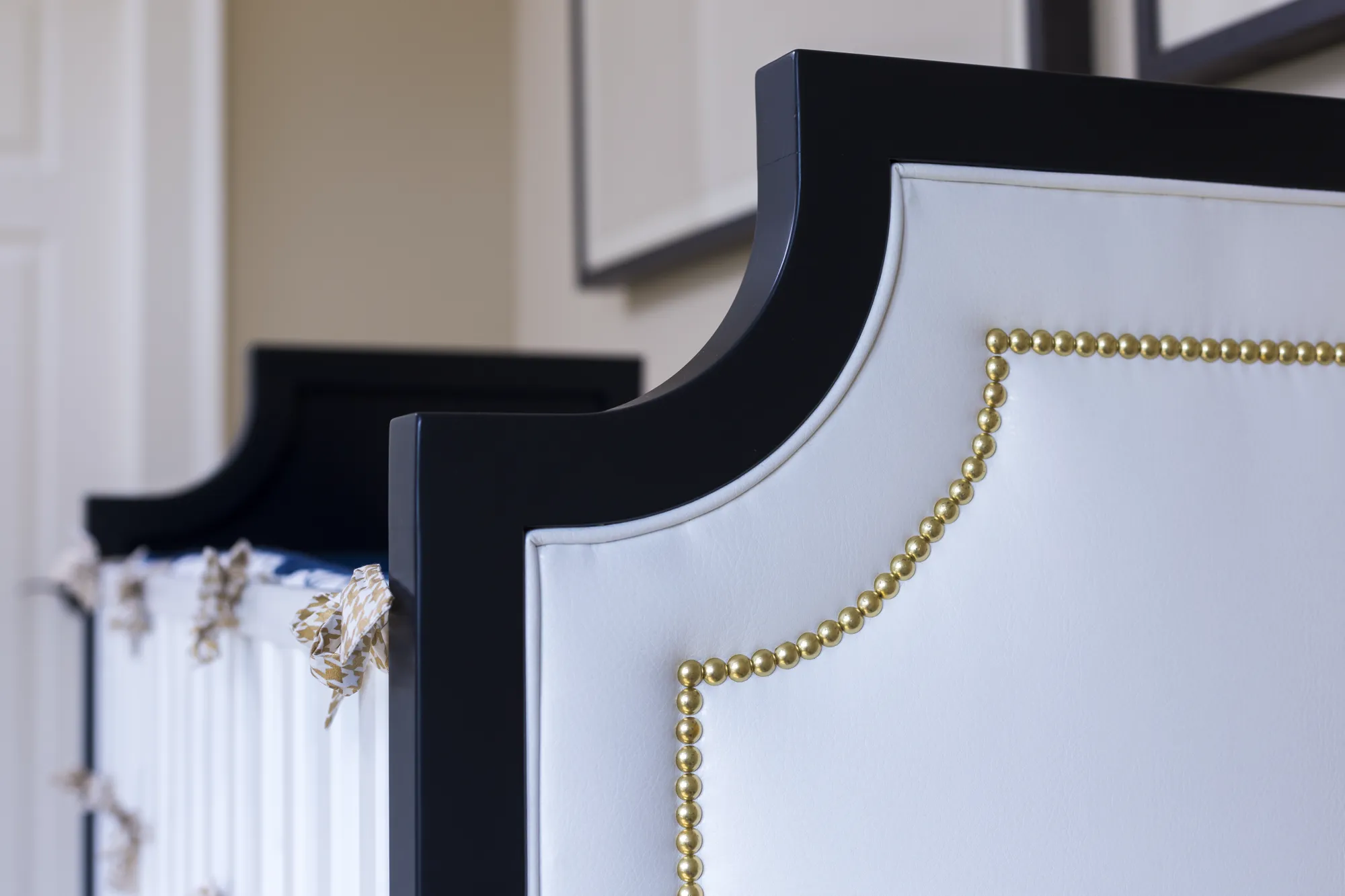 Detailed view of a custom crib with a dark navy frame and white padded upholstery accented with decorative brass nail heads.
