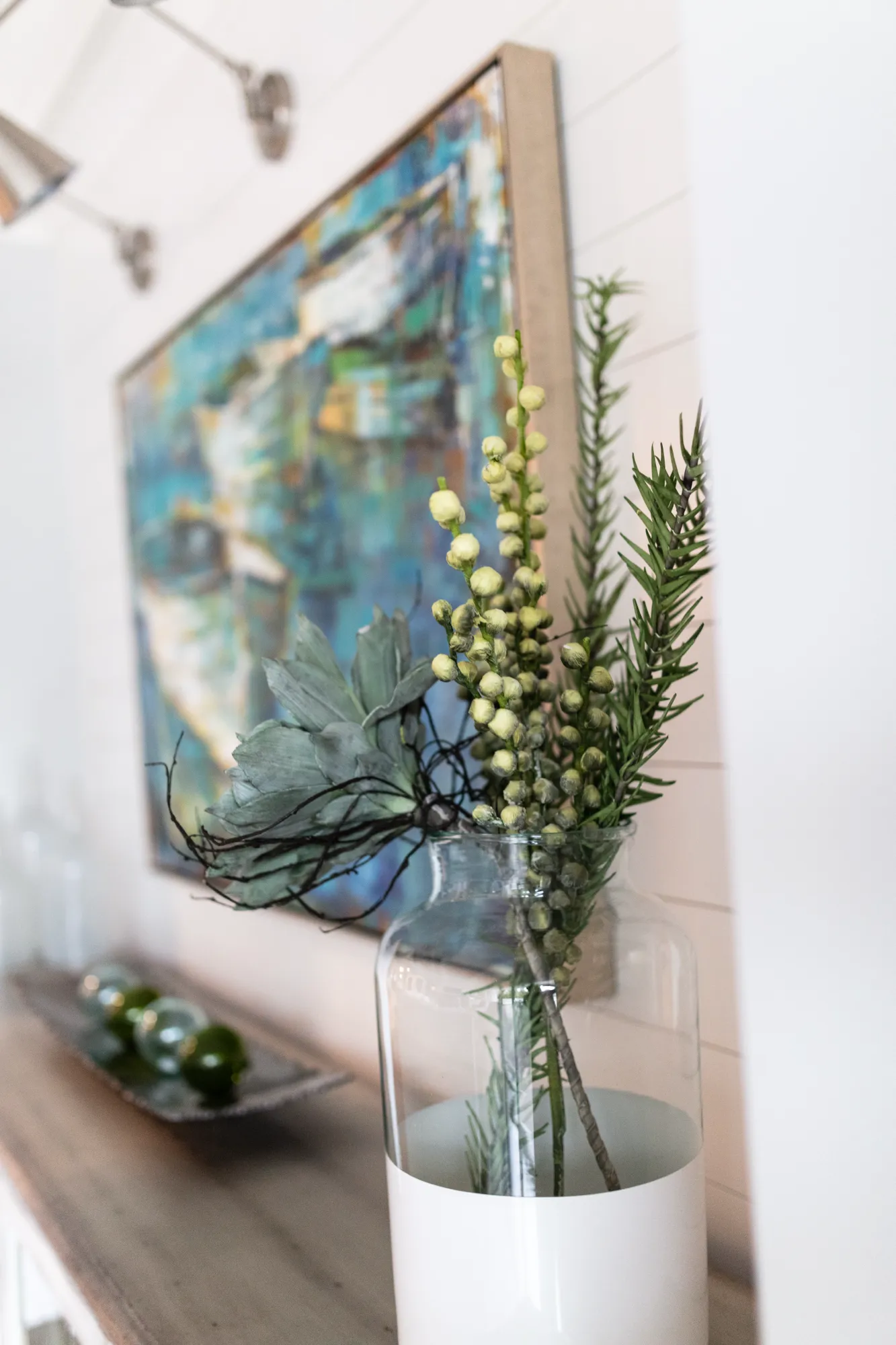 Decorative art objects, including a vase of greenery and an abstract blue painting, displayed against a white shiplap wall.