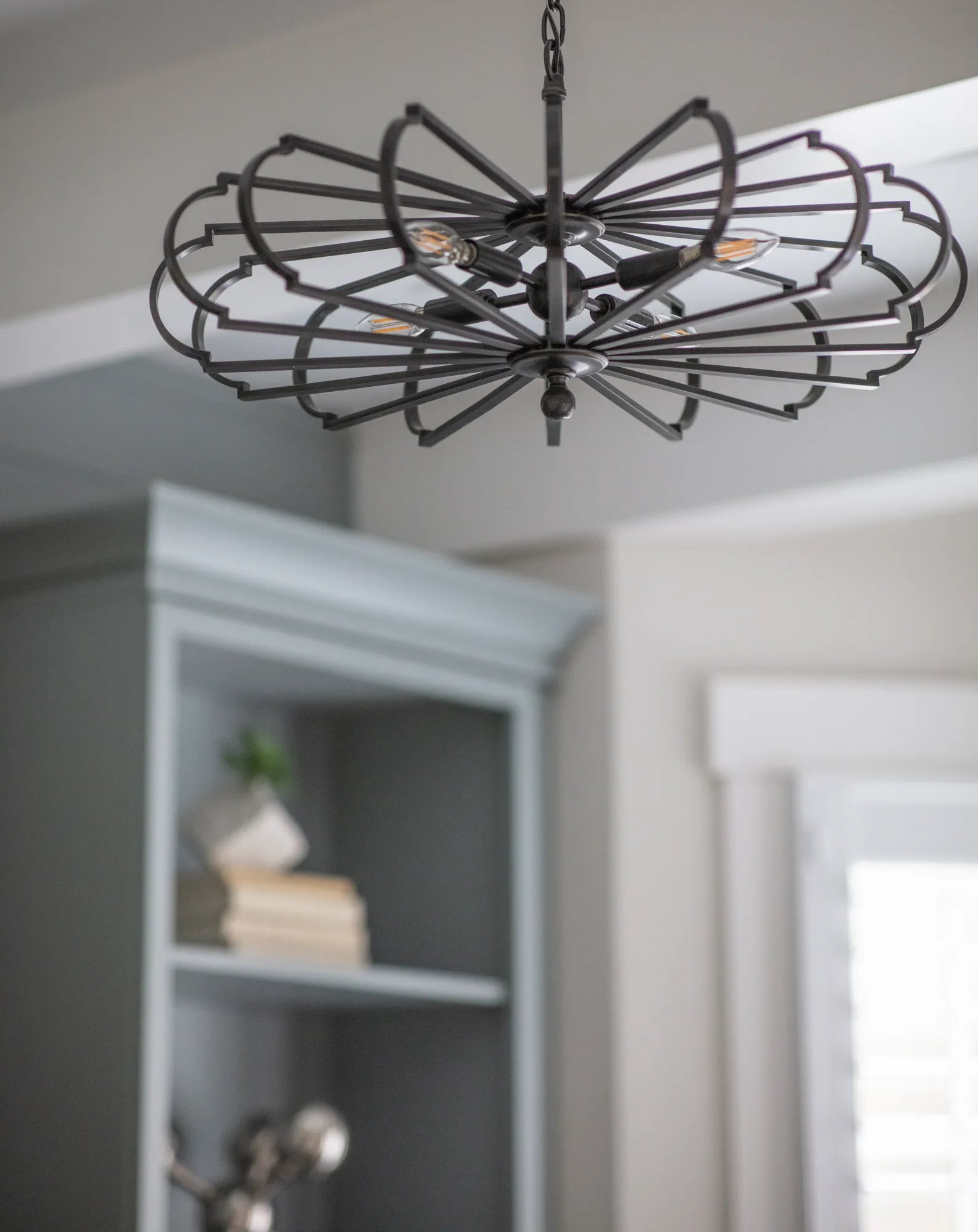 A dark metal, scalloped radial light fixture hangs from the ceiling. In the blurred background, a soft blue built-in bookcase is visible.
