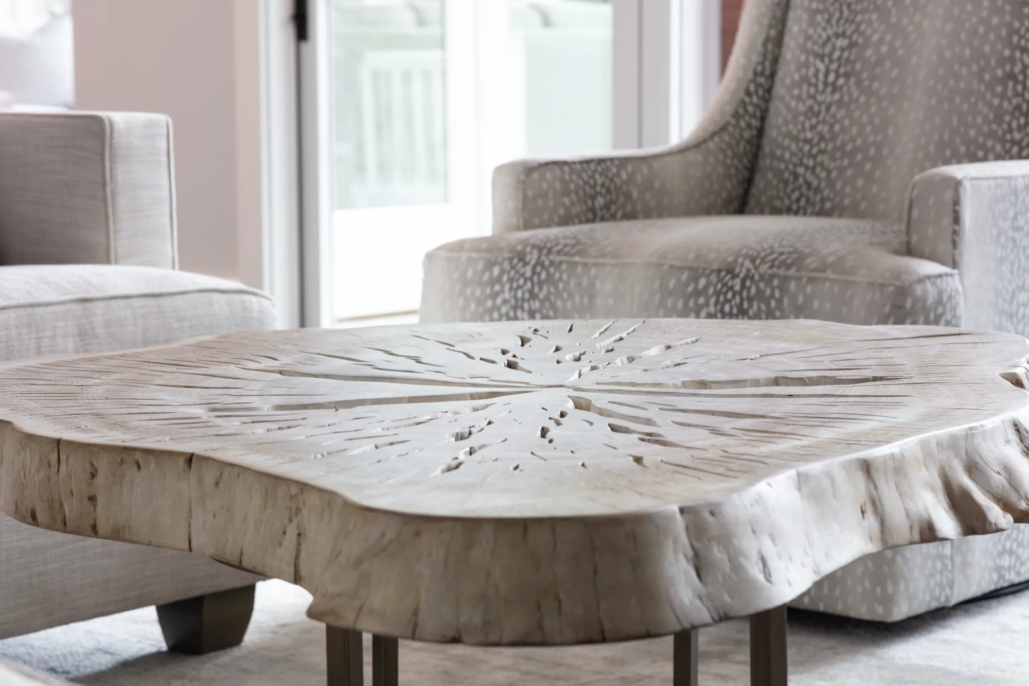 A rustic live-edge wood coffee table with radiating cracks sits between two armchairs, one upholstered in a spotted animal print.