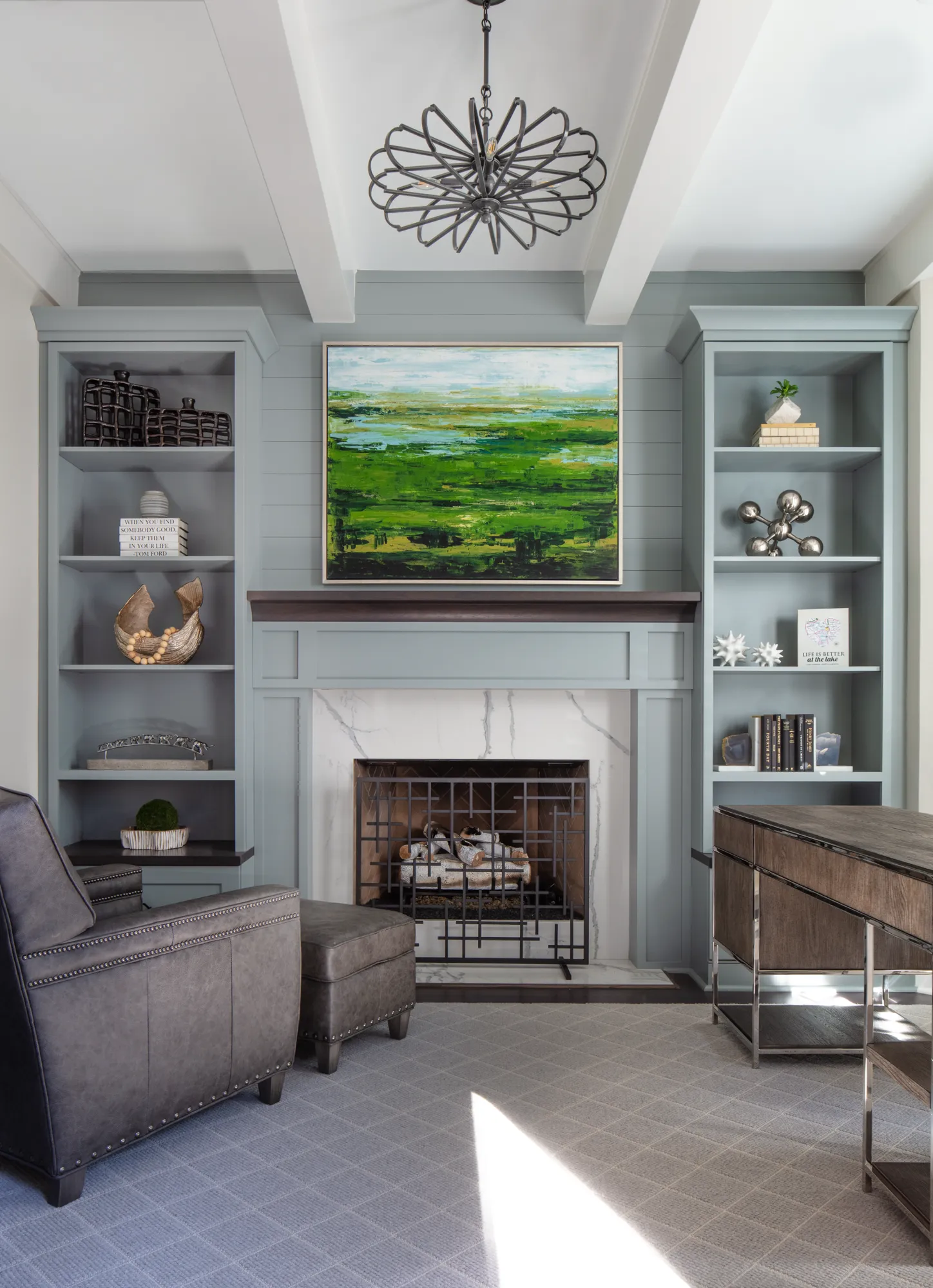 A transitional sitting room features light blue built-in bookshelves and a marble fireplace. A studded leather chair and desk define this peaceful, elegant office space.