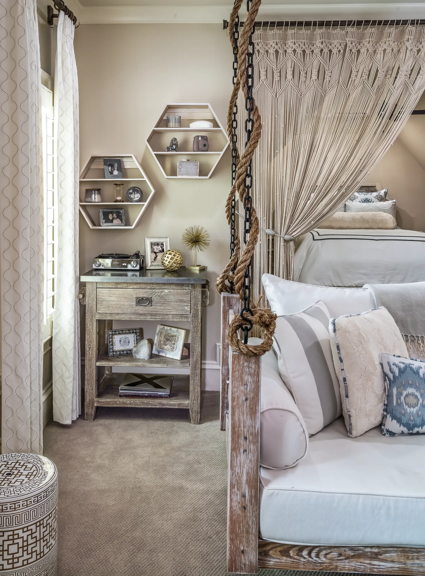 A cozy, rustic bedroom features a suspended daybed with plush pillows, a macrame canopy, and a wooden side table with a record player.