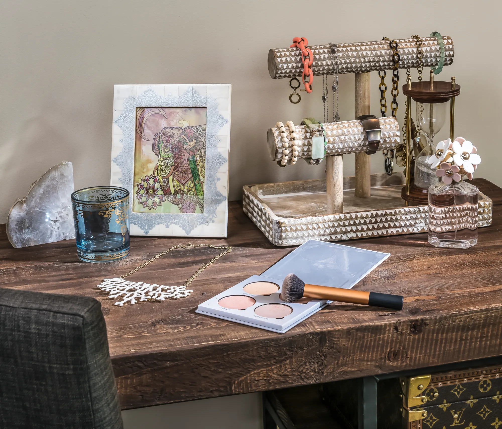 A decorated wooden vanity surface featuring a jewelry display stand, a framed picture, cosmetics, an hourglass, and a large crystal geode.
