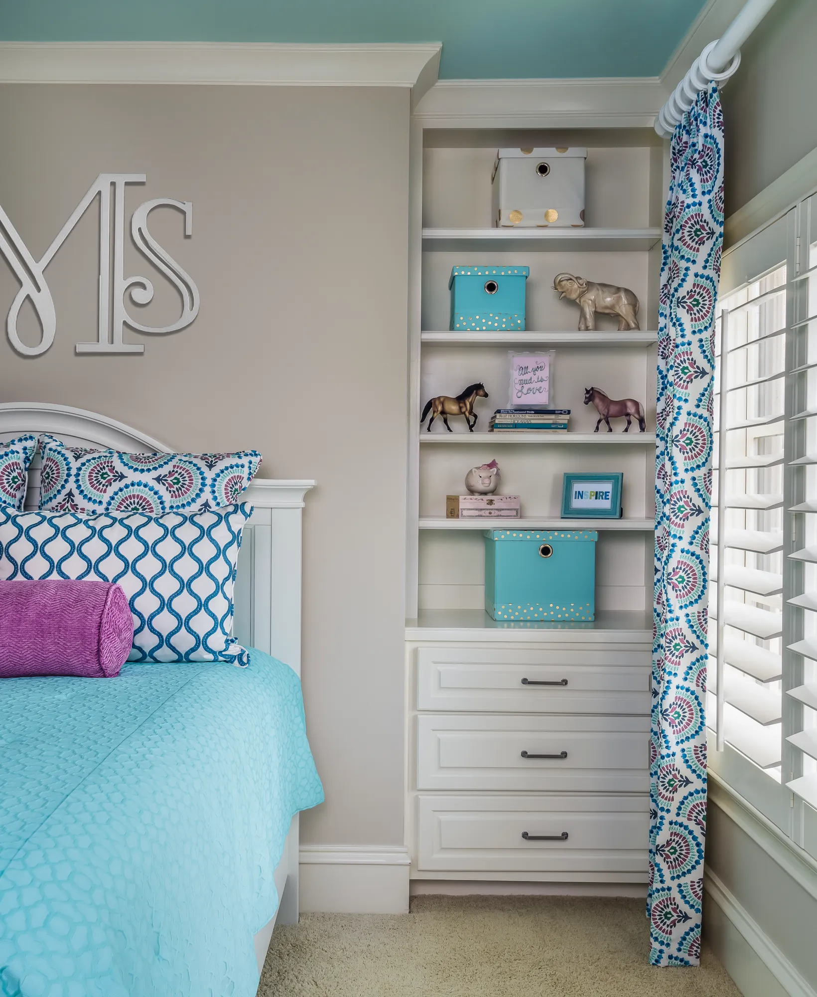 A brightly decorated bedroom corner with turquoise and magenta accents. A white bed sits next to built-in white shelving holding organized storage bins, figurines, and motivational signs.