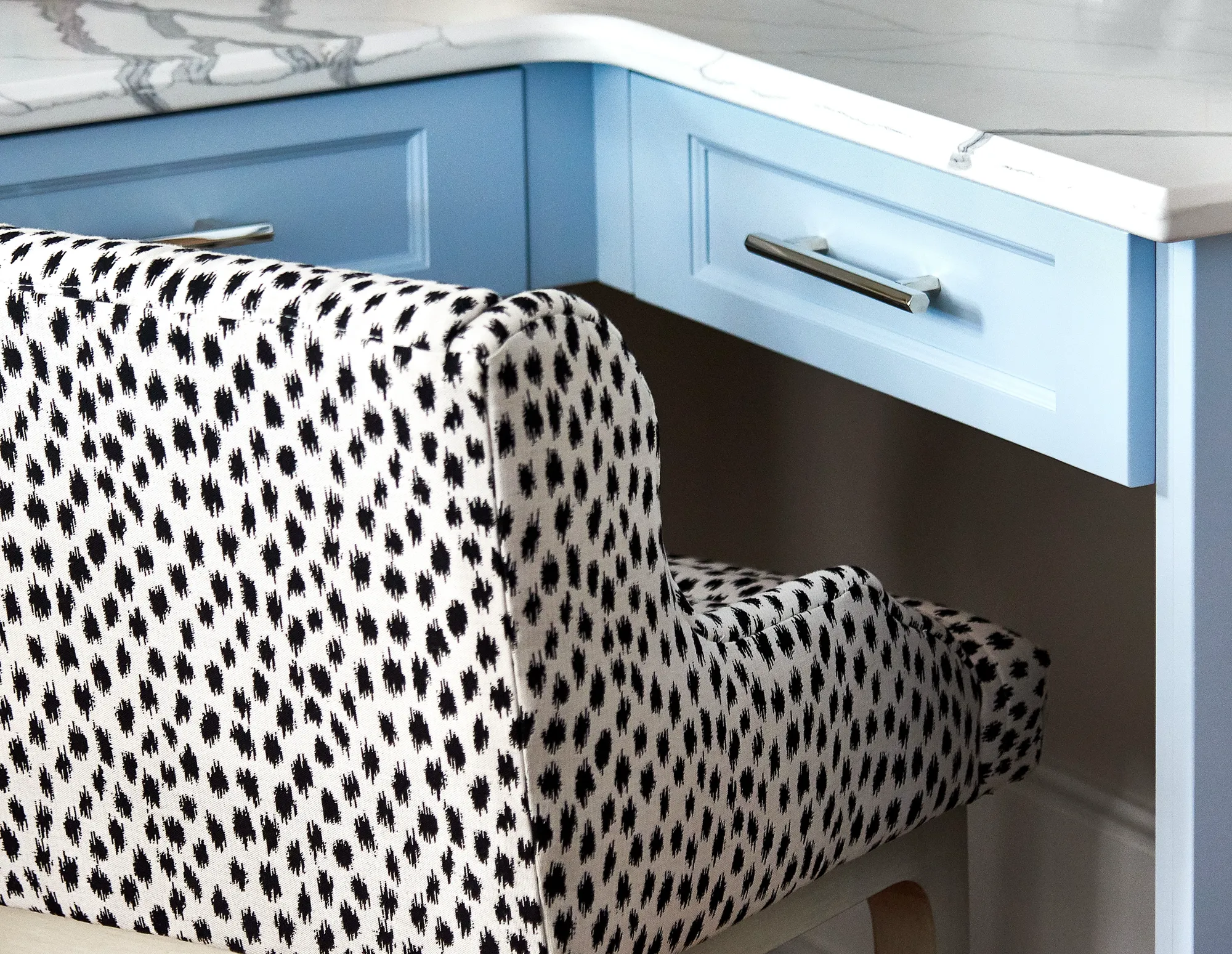 A spotted black and white chair seat is tucked beneath a light blue desk with a marble countertop and silver handles.