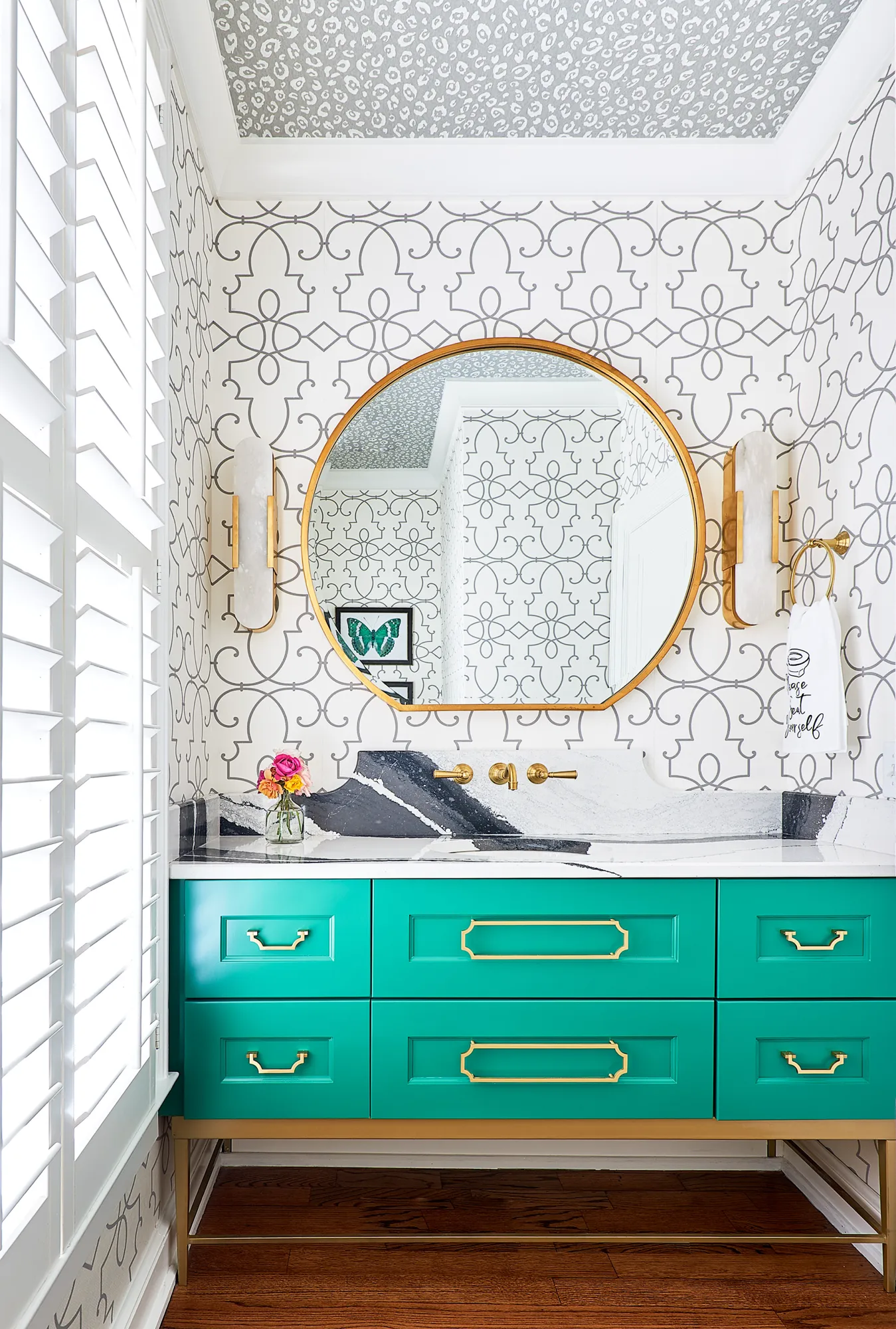 A bold powder room featuring a bright teal vanity, gold hardware, and a striking black and white marble counter. The walls are geometric print, and the ceiling is gray leopard print.