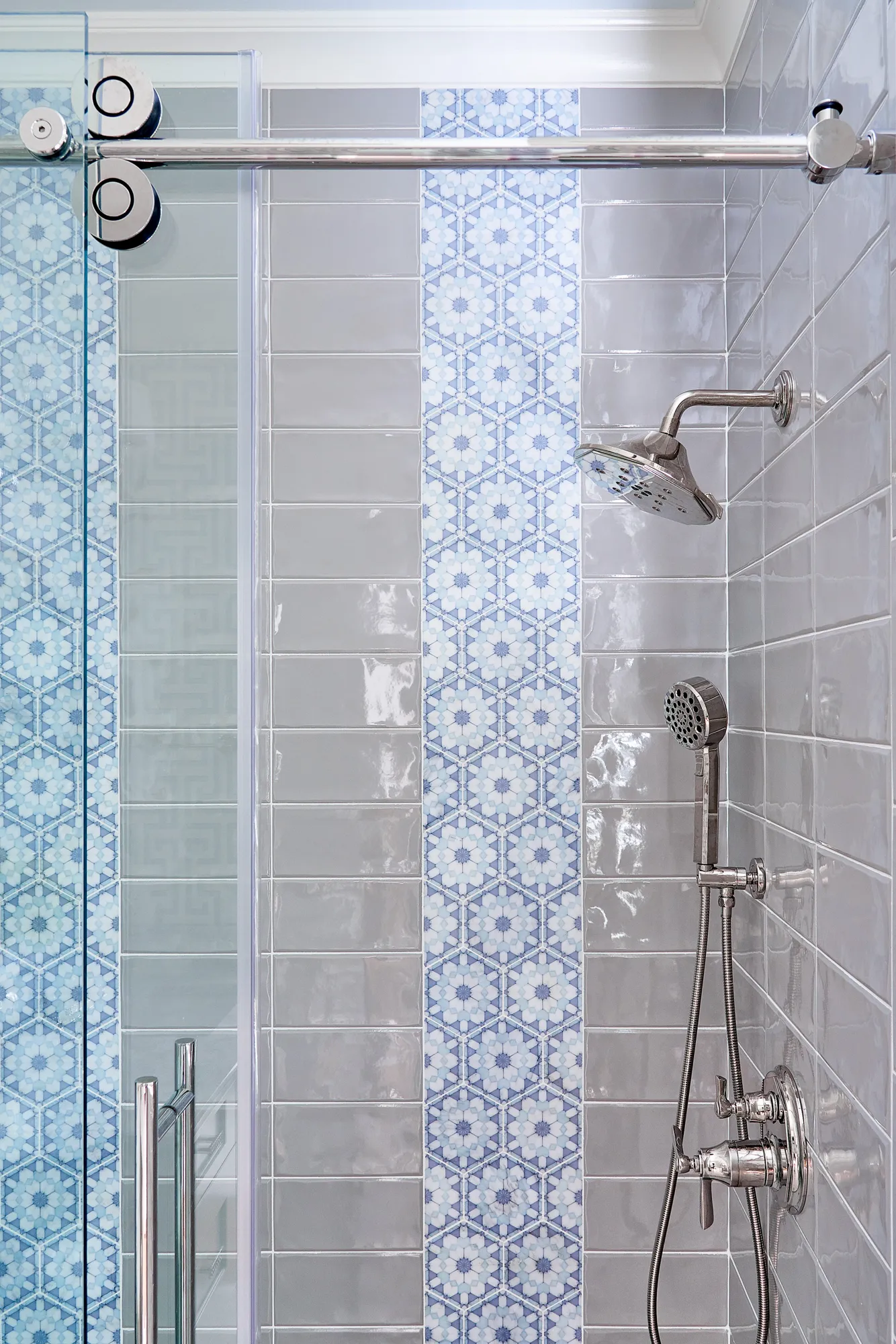 A modern shower featuring glossy gray subway tiles accented by a vertical stripe of blue and white geometric mosaic tile. Chrome fixtures are visible next to the glass door.