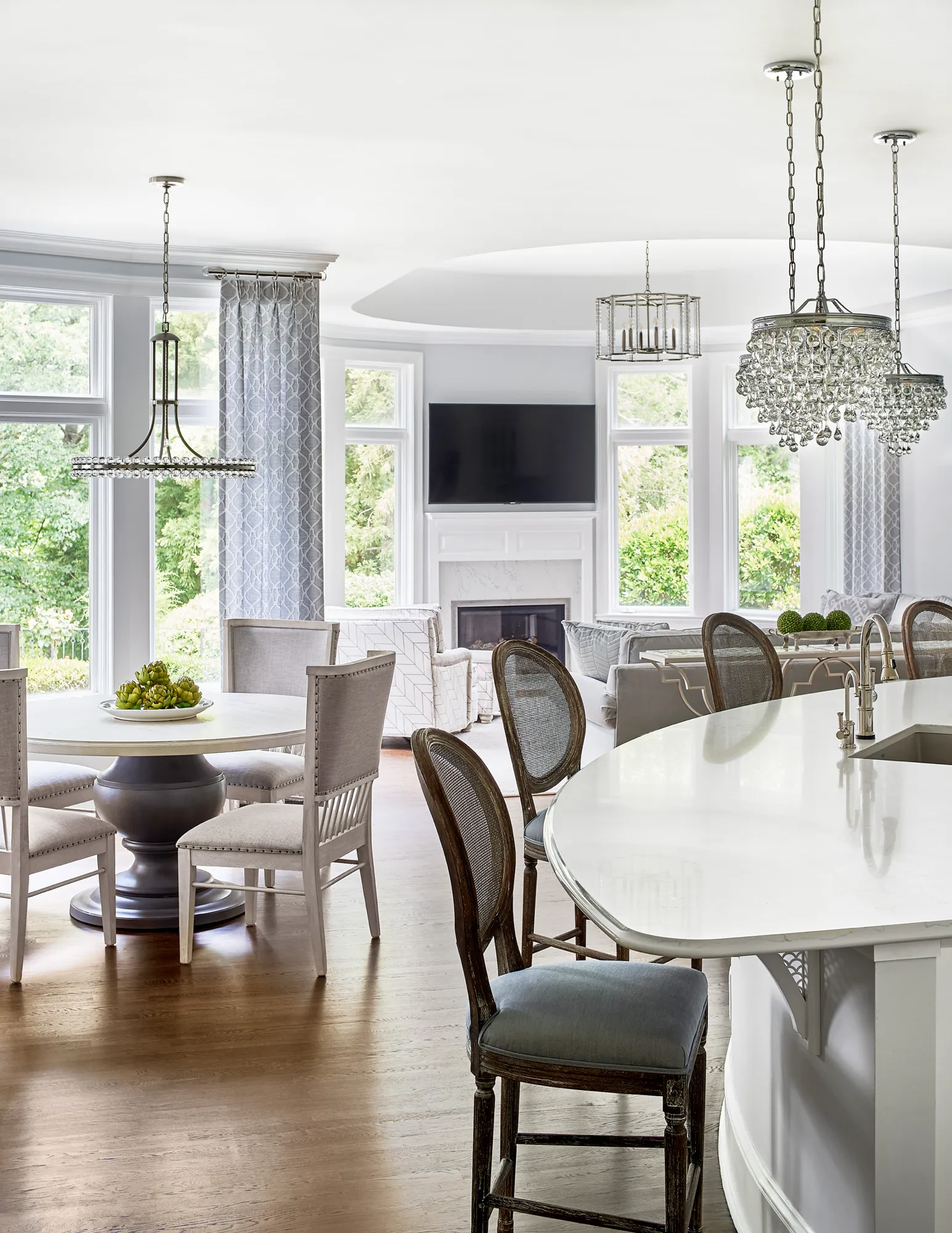 An elegant open-concept living space featuring dark wood floors, a breakfast nook, and a kitchen island, leading into a light-filled living room with a fireplace and large windows.