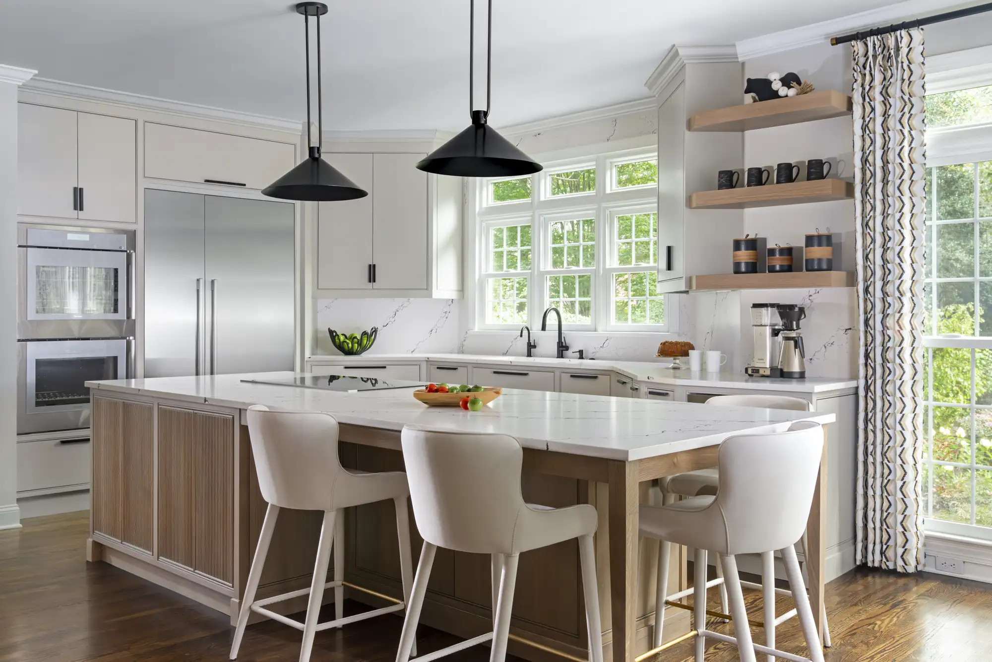 A clean, modern kitchen features light cabinets, a central island with slatted wood paneling, and white marble countertops. Black pendant lights hang over the island.