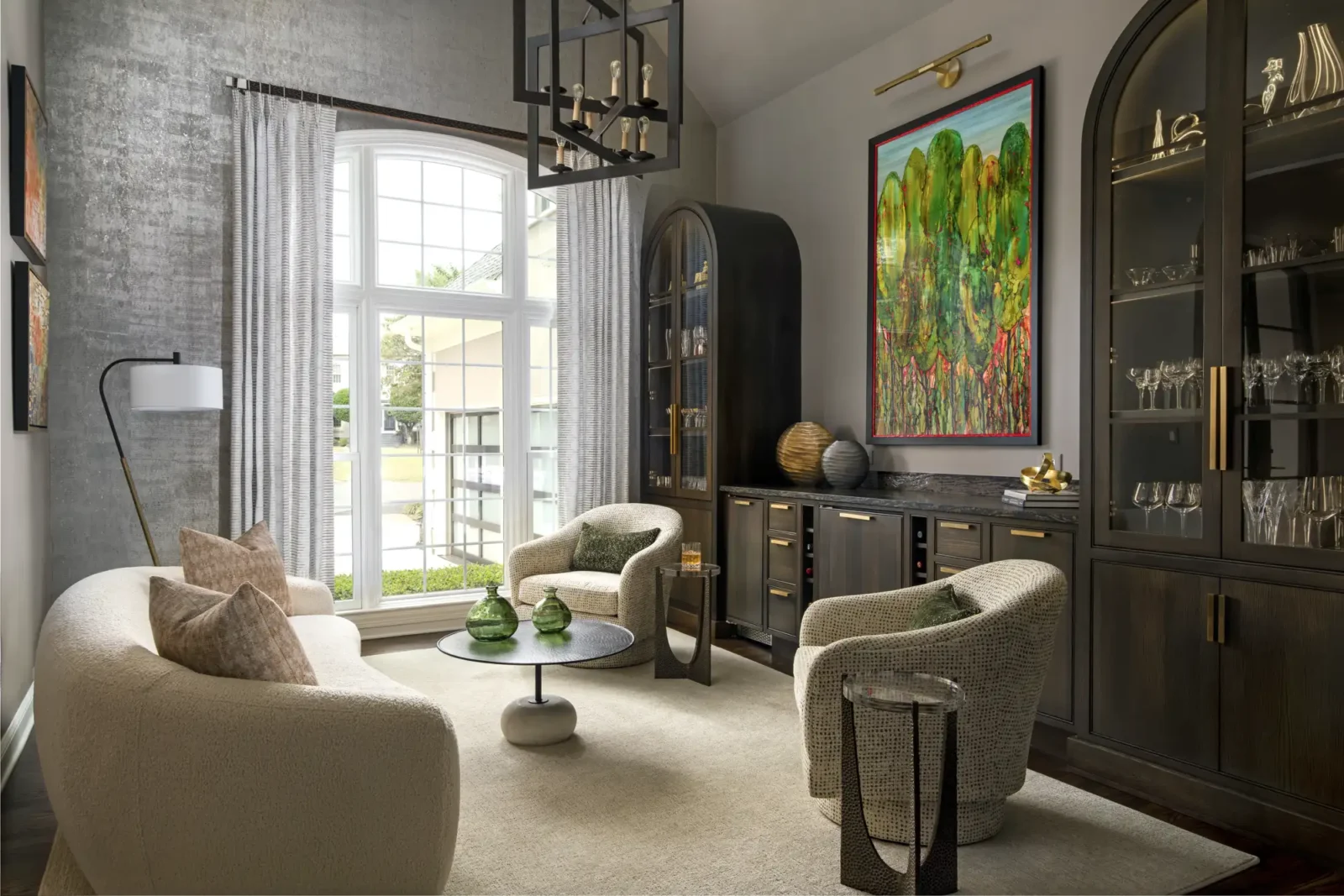 A modern, sophisticated sitting room with a curved white sofa and two textured armchairs arranged around a coffee table near a dark wood bar cabinet.