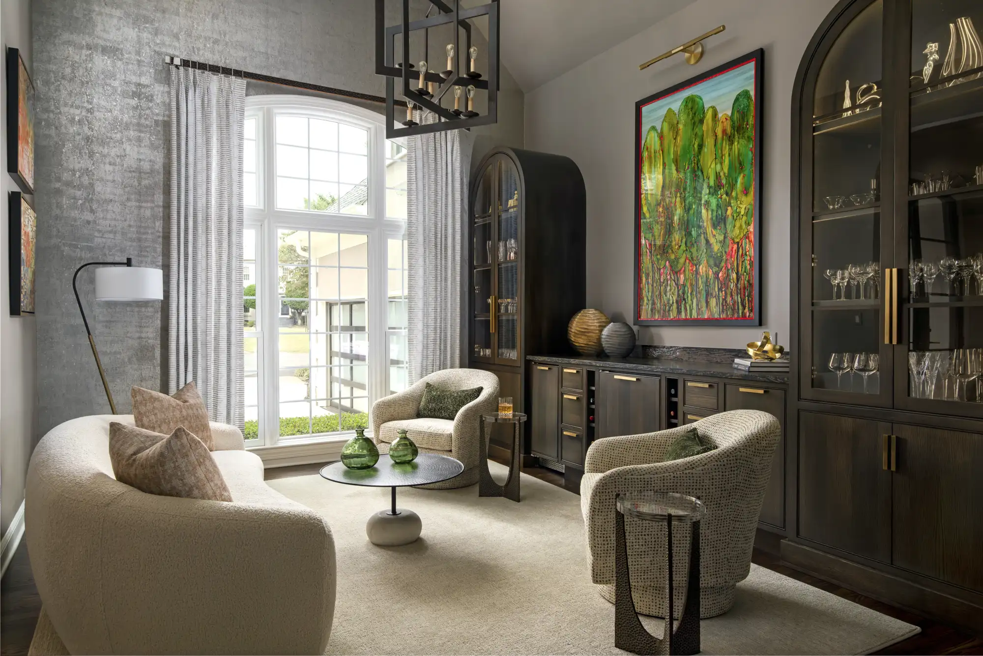 A modern, sophisticated sitting room with a curved white sofa and two textured armchairs arranged around a coffee table near a dark wood bar cabinet.