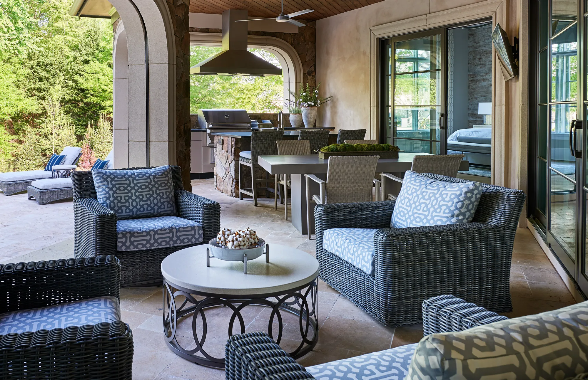 A sophisticated covered patio featuring a full outdoor kitchen, a dining table, and a comfortable seating arrangement with patterned cushions.