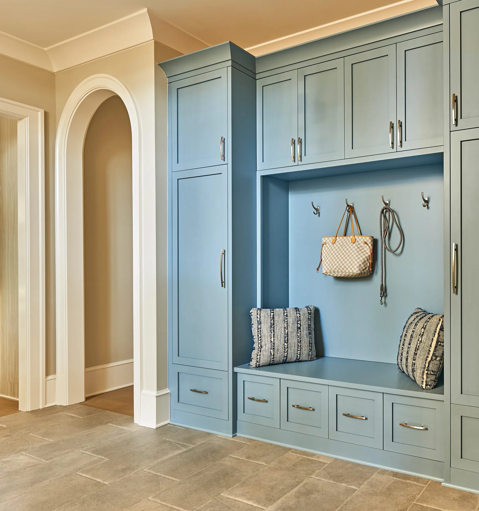 A custom slate-blue mudroom system featuring storage cabinets, a bench, and lower drawers. A tote bag and leash hang in the recessed cubby area.