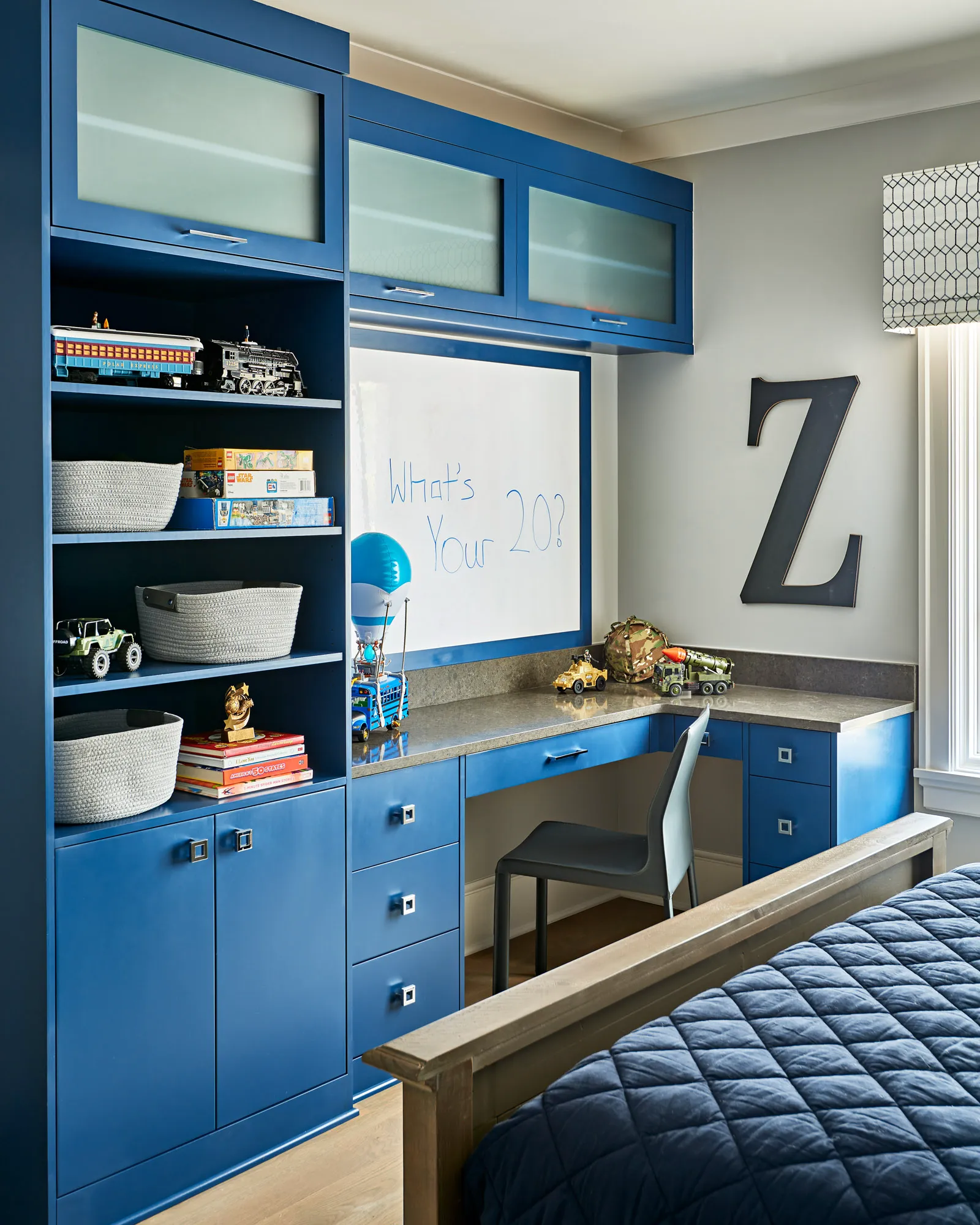 A child's room featuring custom, deep blue built-in cabinetry with shelving, a desk, and a whiteboard. The shelves are neatly organized with toys and books.