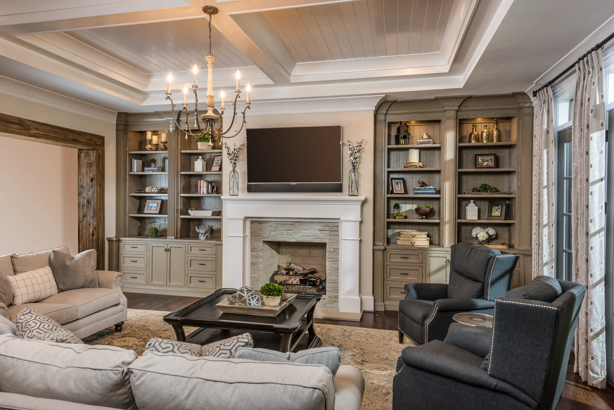 An elegant living room showcasing built-in gray-toned bookshelves flanking a white fireplace and a mounted television, with comfortable couches and armchairs.