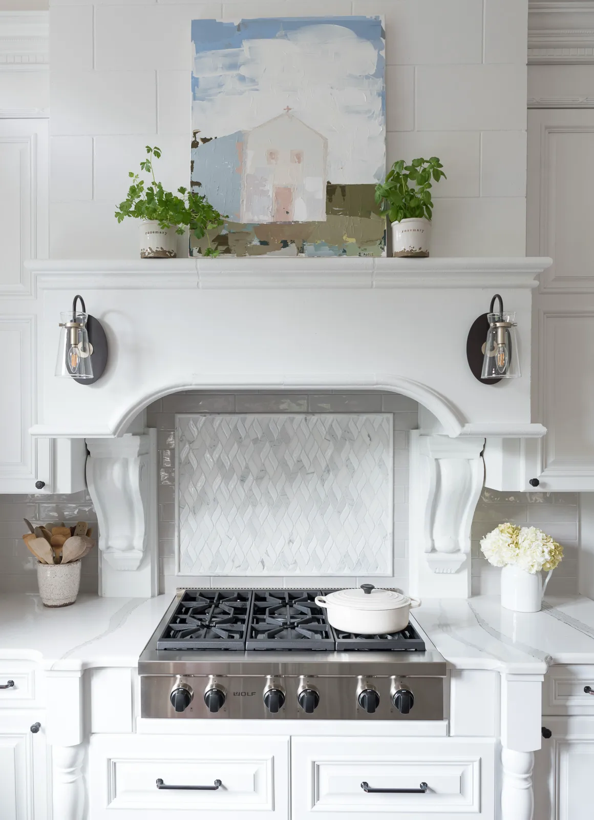 A white custom kitchen featuring a professional range, marble countertops, and an ornate white range hood with a mosaic tile backsplash.