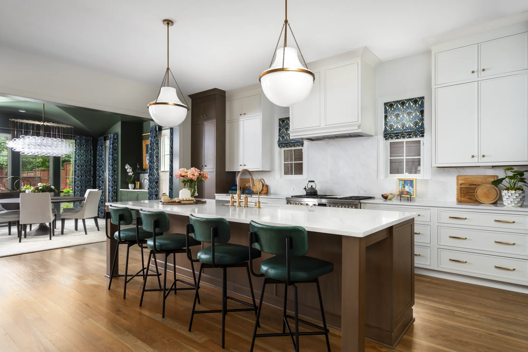 A bright kitchen featuring a brown island with emerald green stools and white upper cabinets opens to a dramatic, dark green dining area.